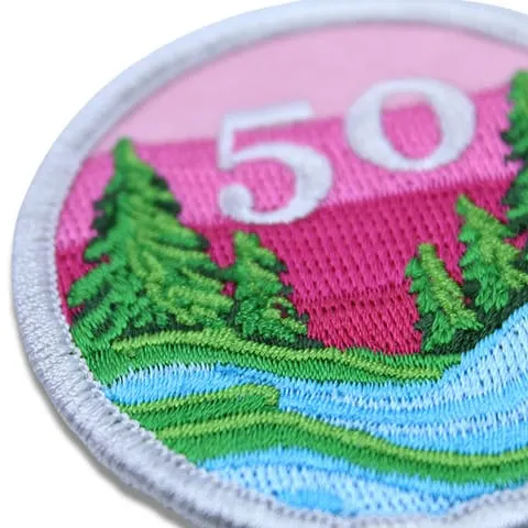 Close up image of an embroidered patch with trees and pink background