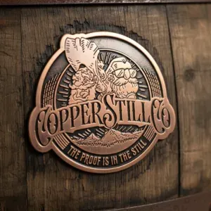 Custom copper distillery emblem displayed on wooden barrel